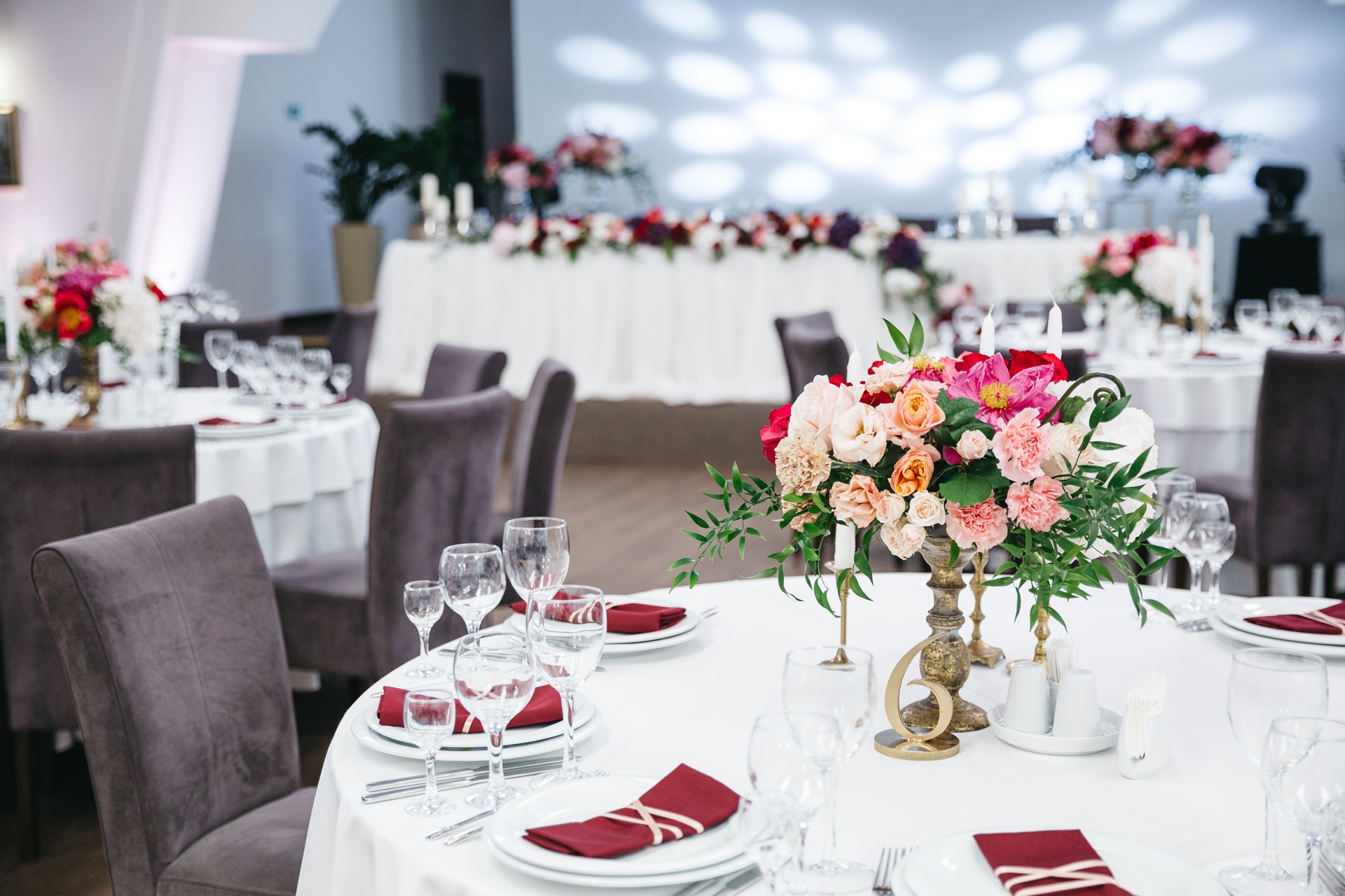 Elegant reception hall with round tables, blush floral centerpieces and burgundy-accented place settings