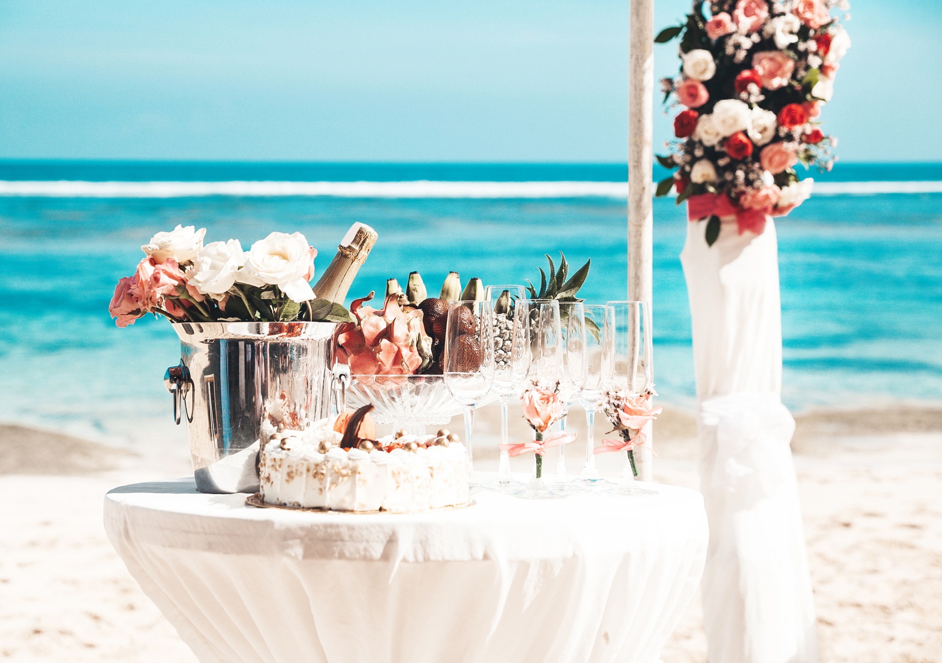 Champagne, cake and tropical fruit styled on a beachside dessert table overlooking the ocean