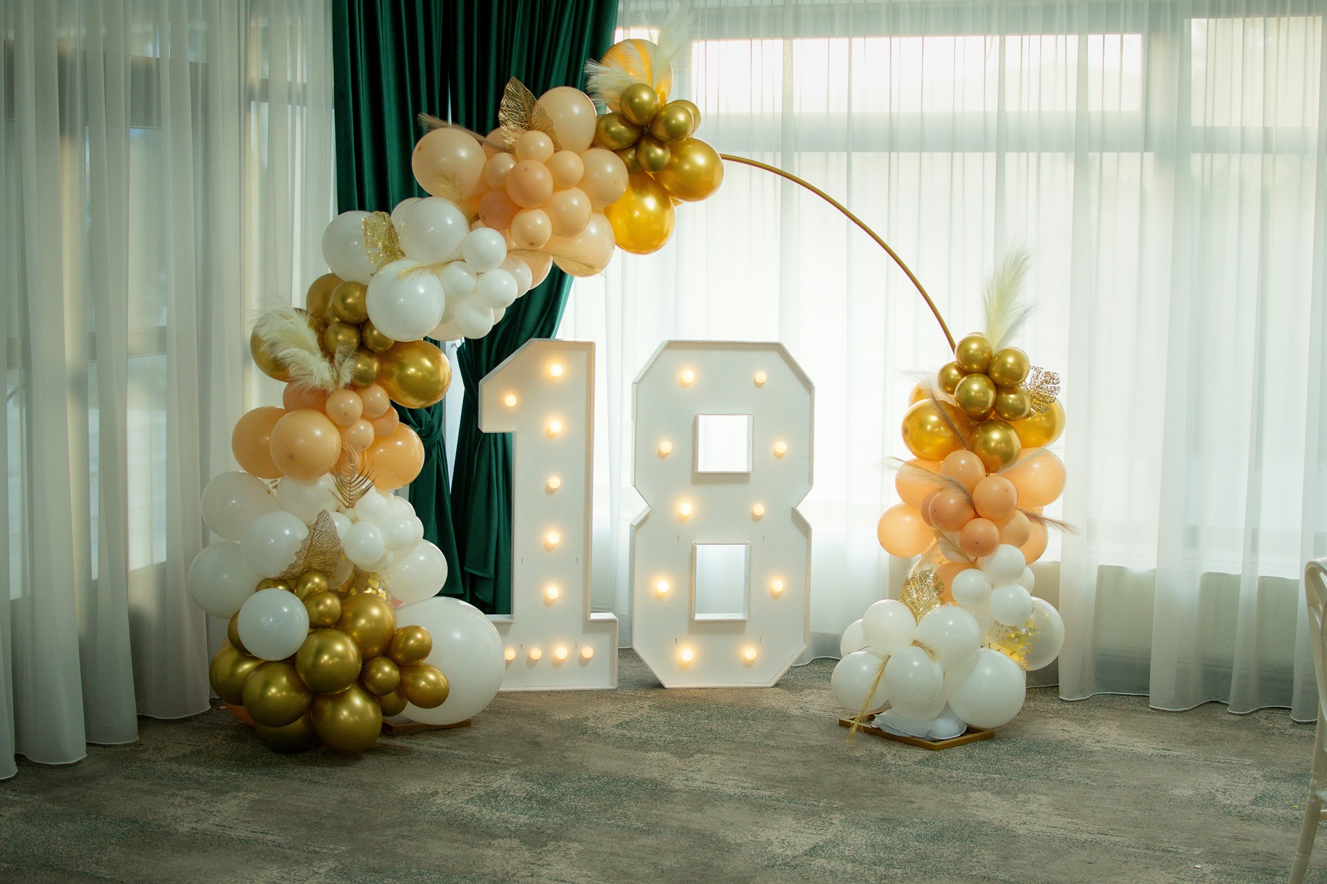 Gold and white balloon garland arch framing light-up '18' marquee numbers for a milestone birthday