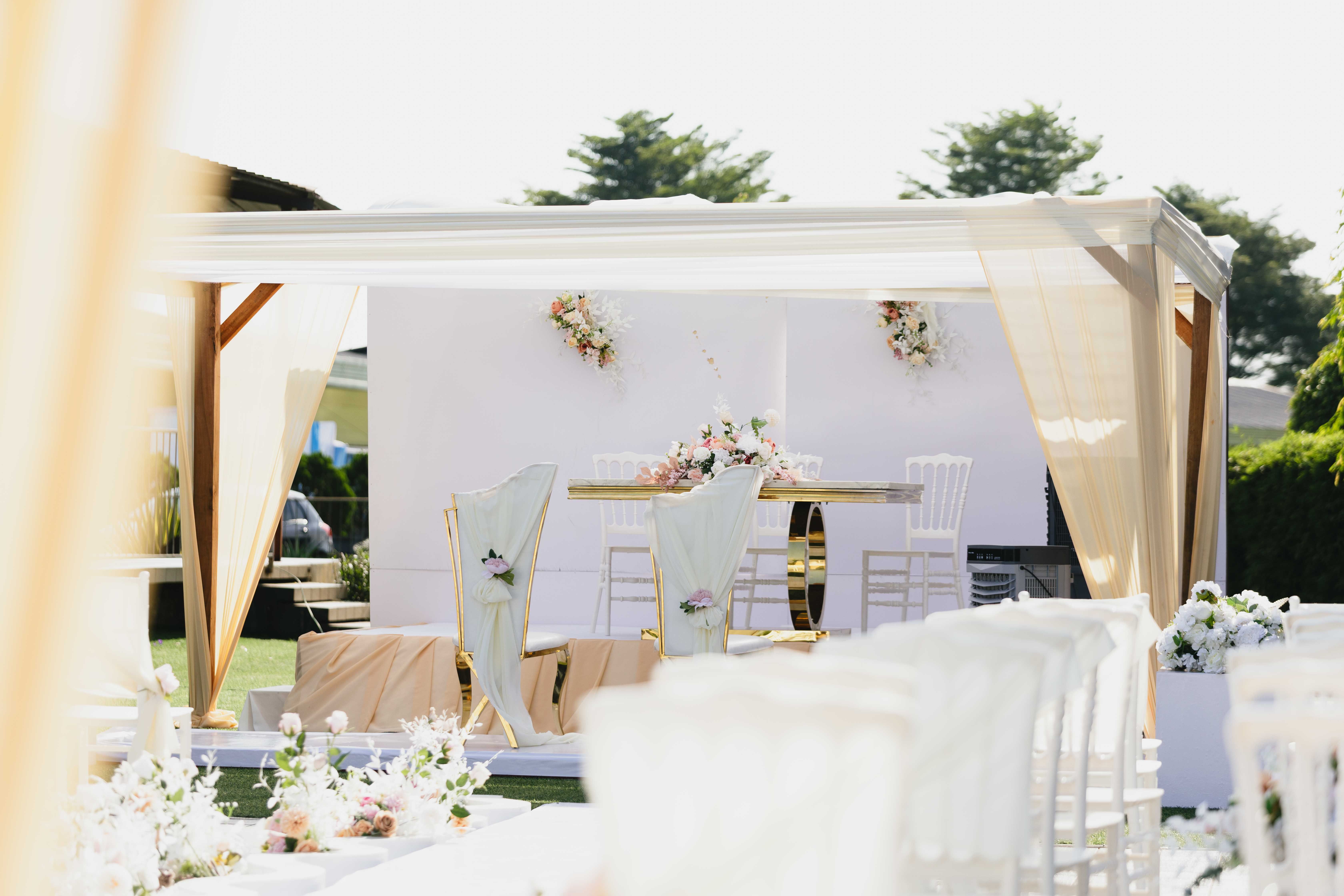 Draped outdoor pavilion with a floral sweetheart table and aisle seating ready for a ceremony