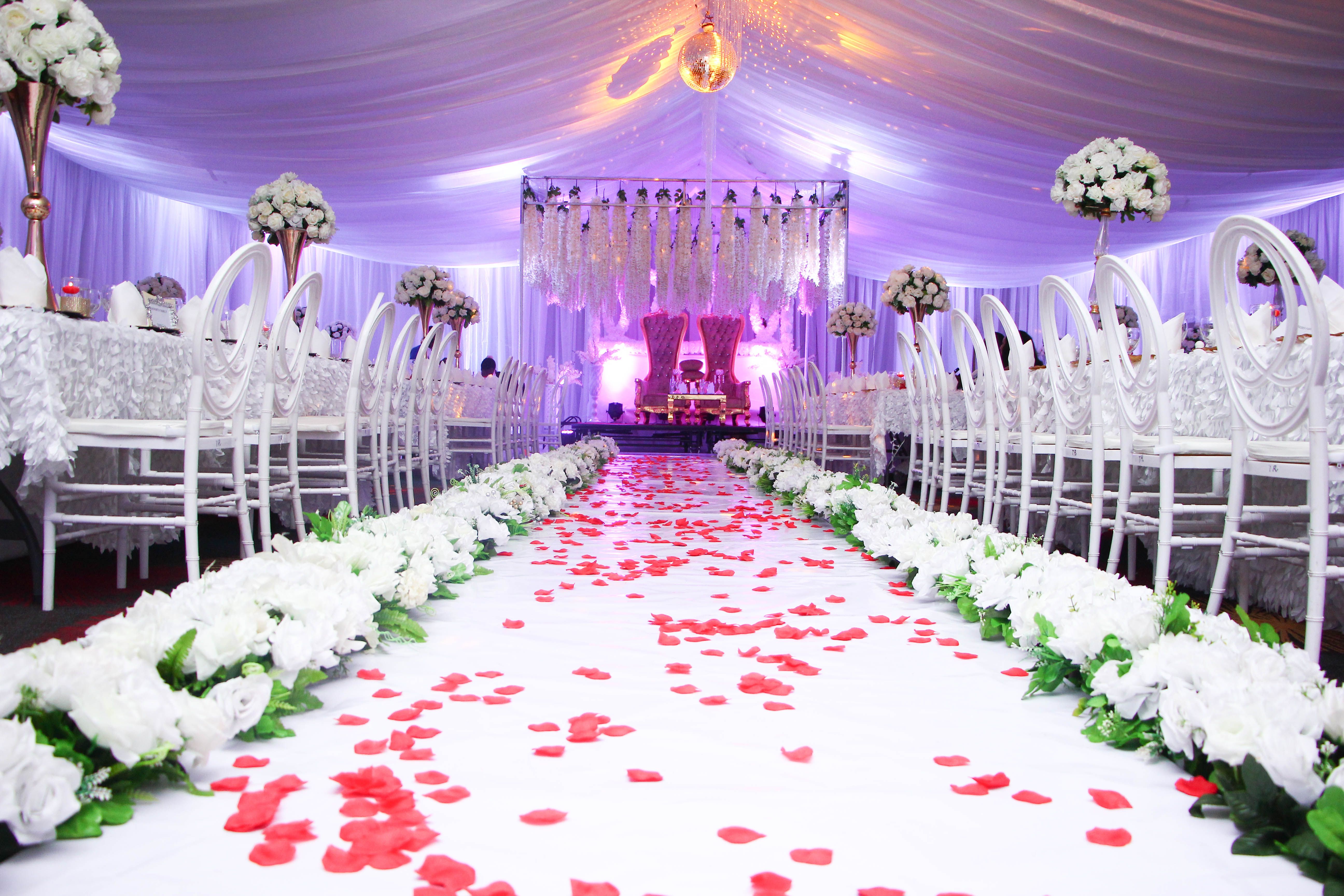 Wide view of an elegant wedding reception hall with crystal chandeliers, string lights, and gold chiavari chairs at candlelit floral-dressed tables